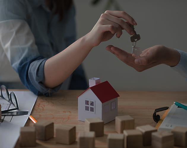 Real Estate Property Handover – Key Exchange in Successful Transaction Hands exchanging house keys over model home on table symbolizing real estate transaction.